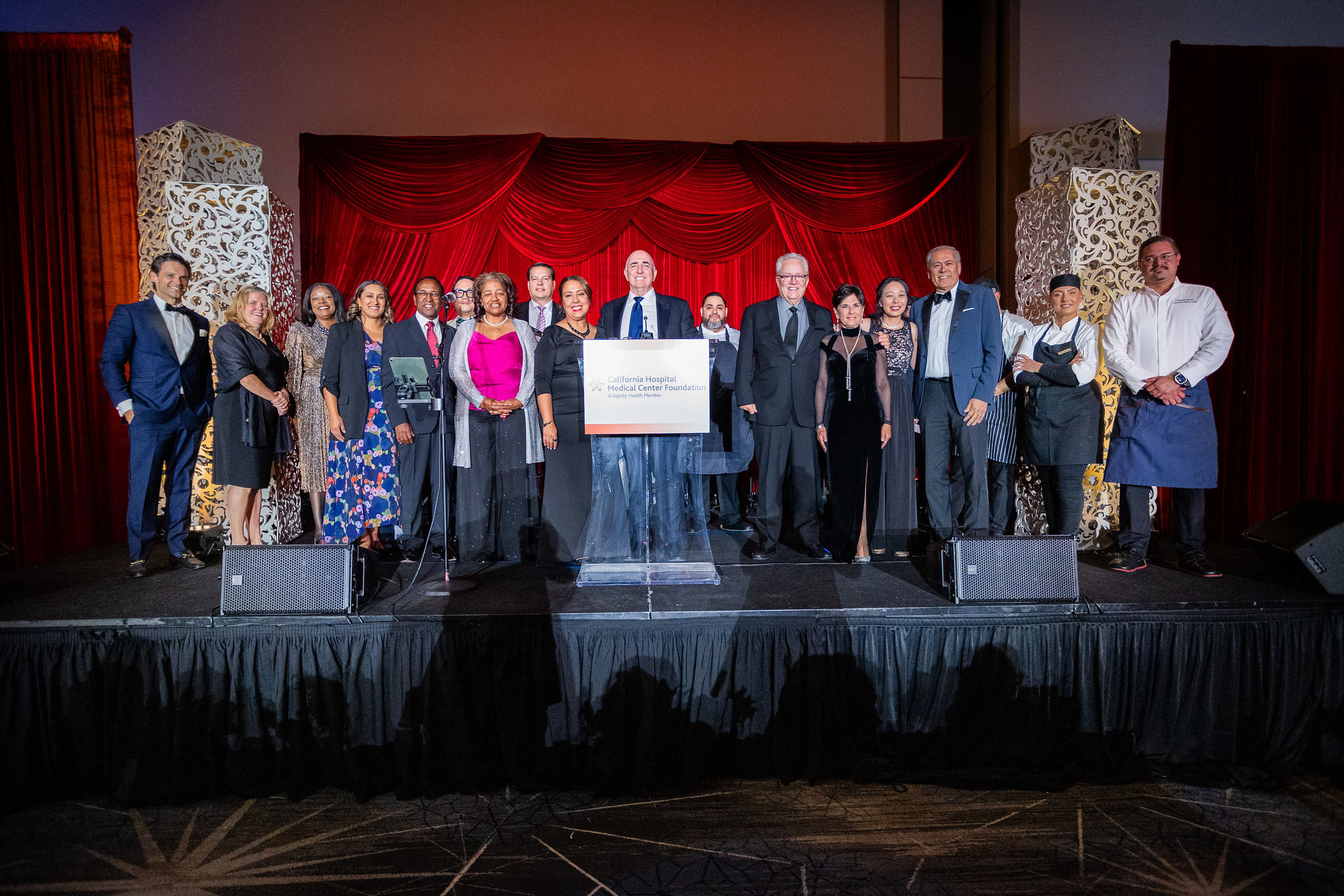 Group photo of La Grande Affaire planning committee, California Hospital medical staff, board members and JW Marriott culinary team standing on stage