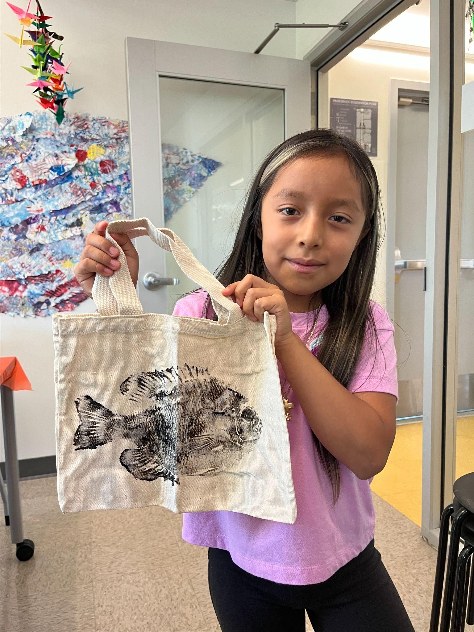 A student displays her finished gyotaku print on her canvas tote bag